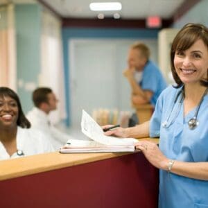 A woman in blue scrubs standing at the front of a hospital.