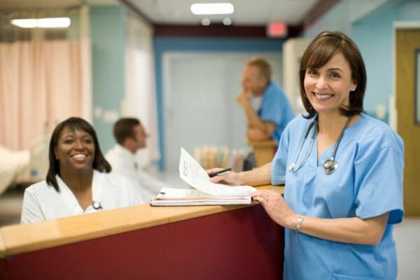 A woman in blue scrubs standing at the front of a hospital.