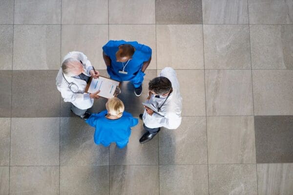 Three doctors are standing on the floor and one is holding a clipboard.