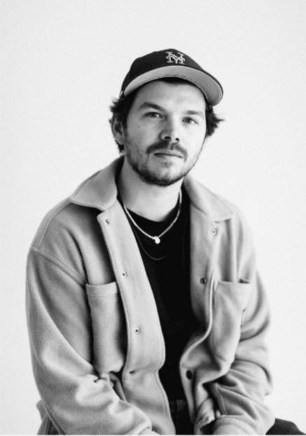 A man in a hat and jacket sitting down.